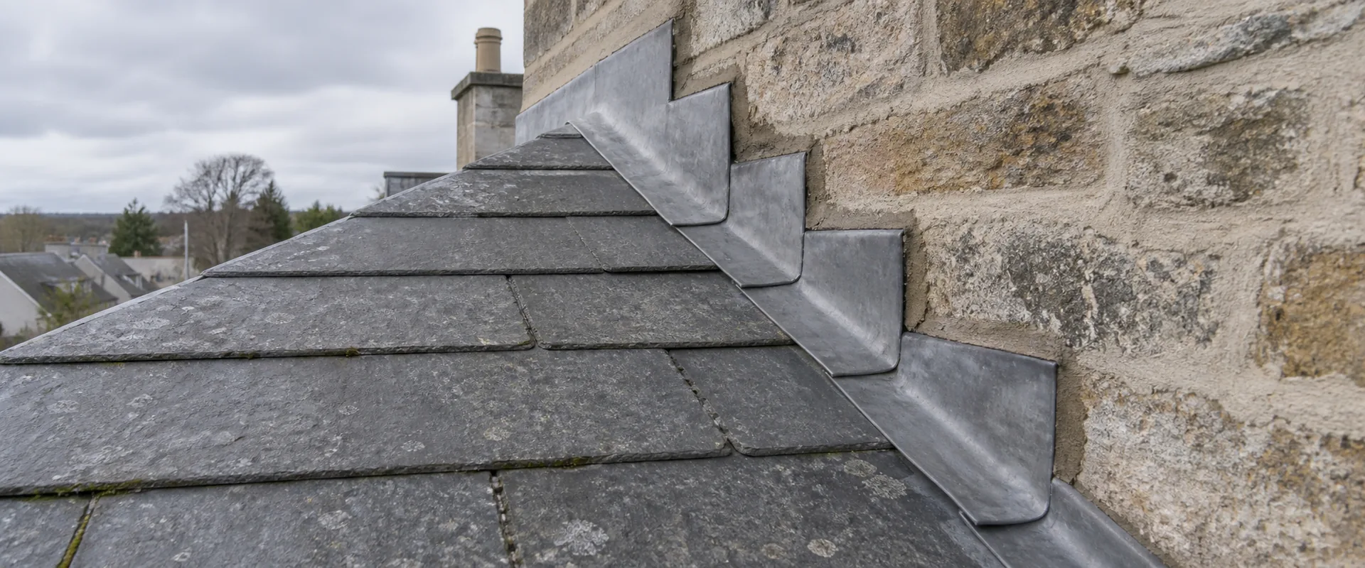 Illustrative stepped lead flashing at the junction of a slate roof and stone wall.