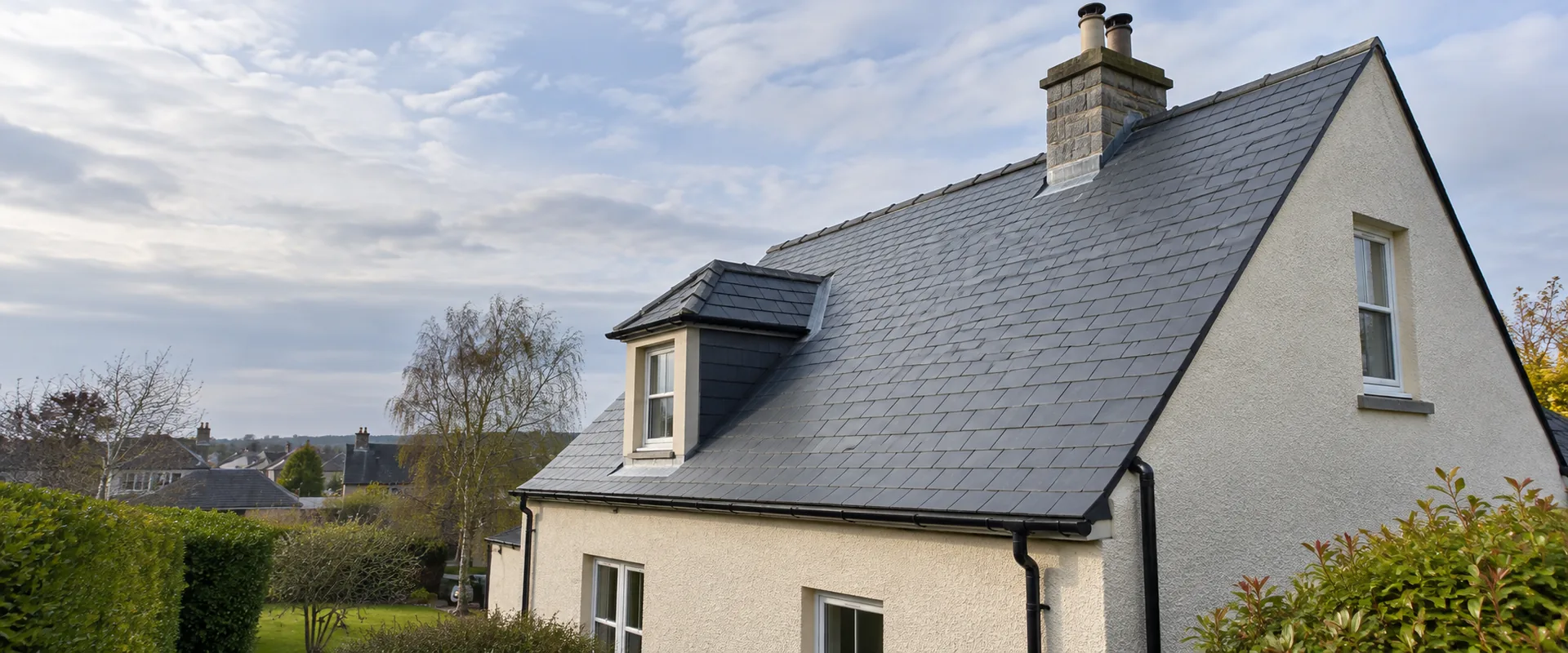 Illustrative newly laid slate roof with black gutters on a cream-harled house.