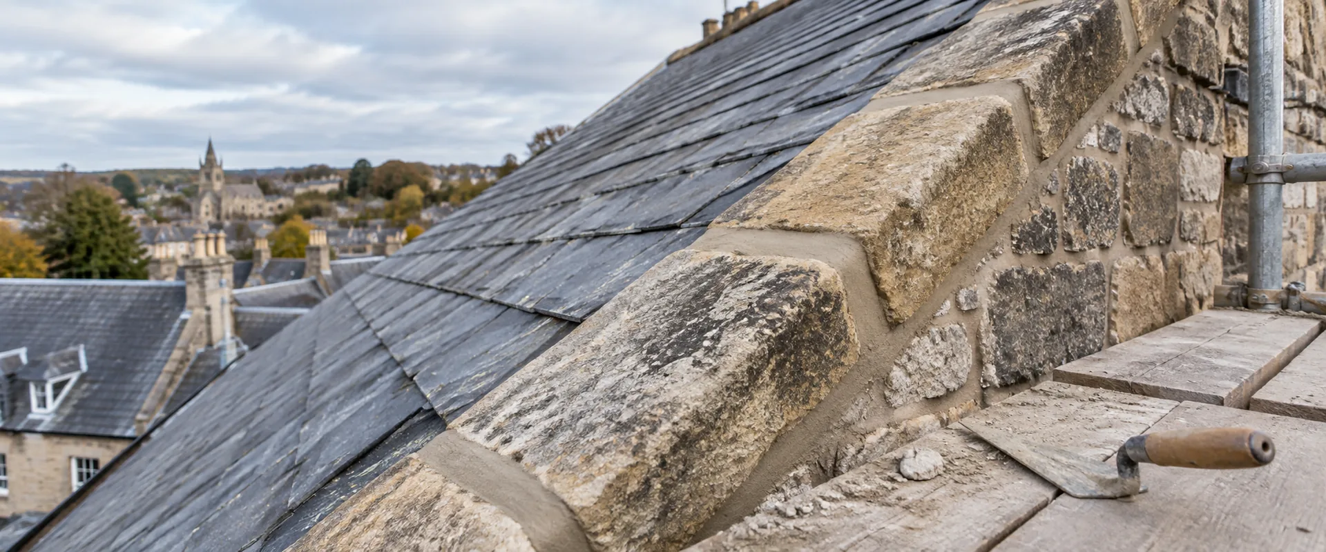 Illustrative repointed mortar joints between stone coping pieces at a slate-roof verge.