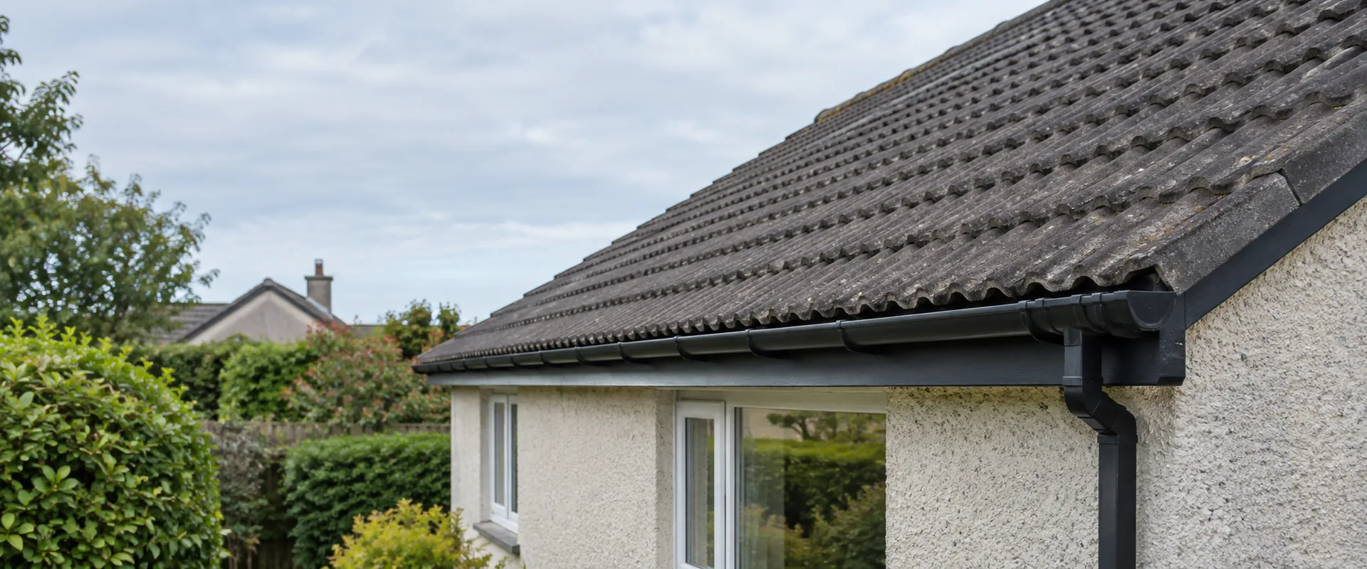 Illustrative interlocking concrete roof tiles and black gutter on a roughcast bungalow.